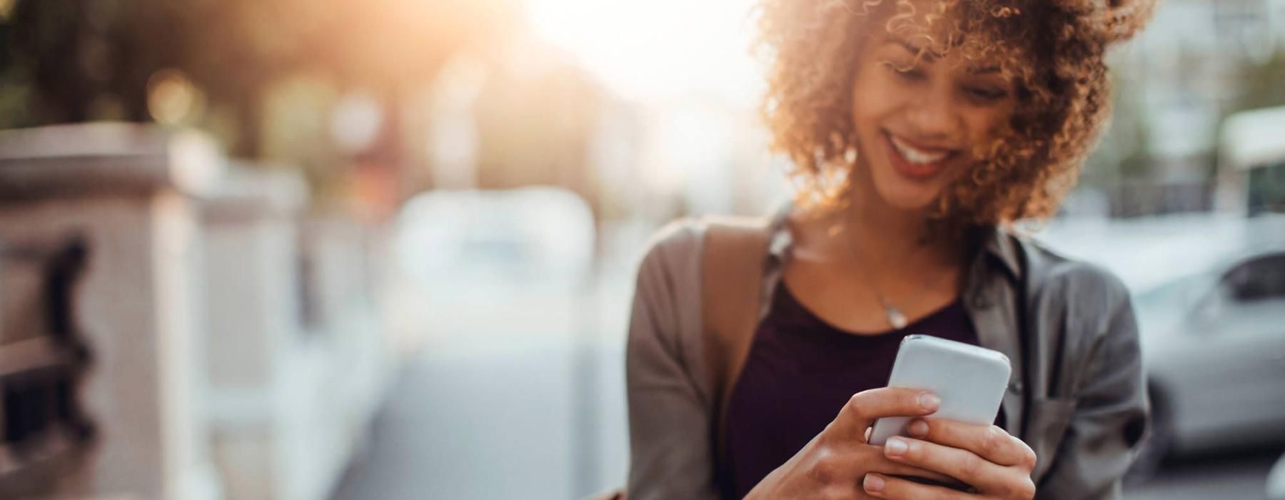 woman texts on her phone as she walks through the city